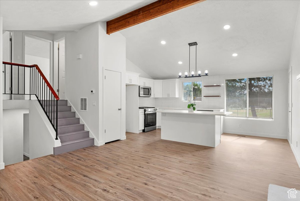 Kitchen featuring decorative light fixtures, a kitchen island, appliances with stainless steel finishes, and light wood-type flooring