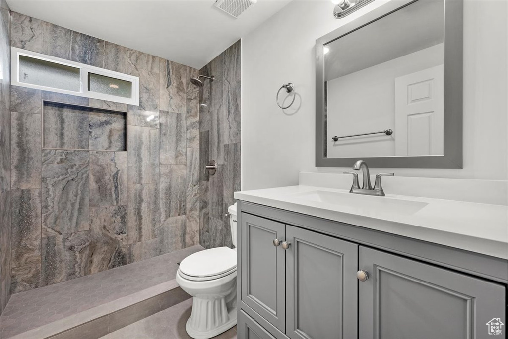 Bathroom with tile patterned floors, vanity, a tile shower, and toilet