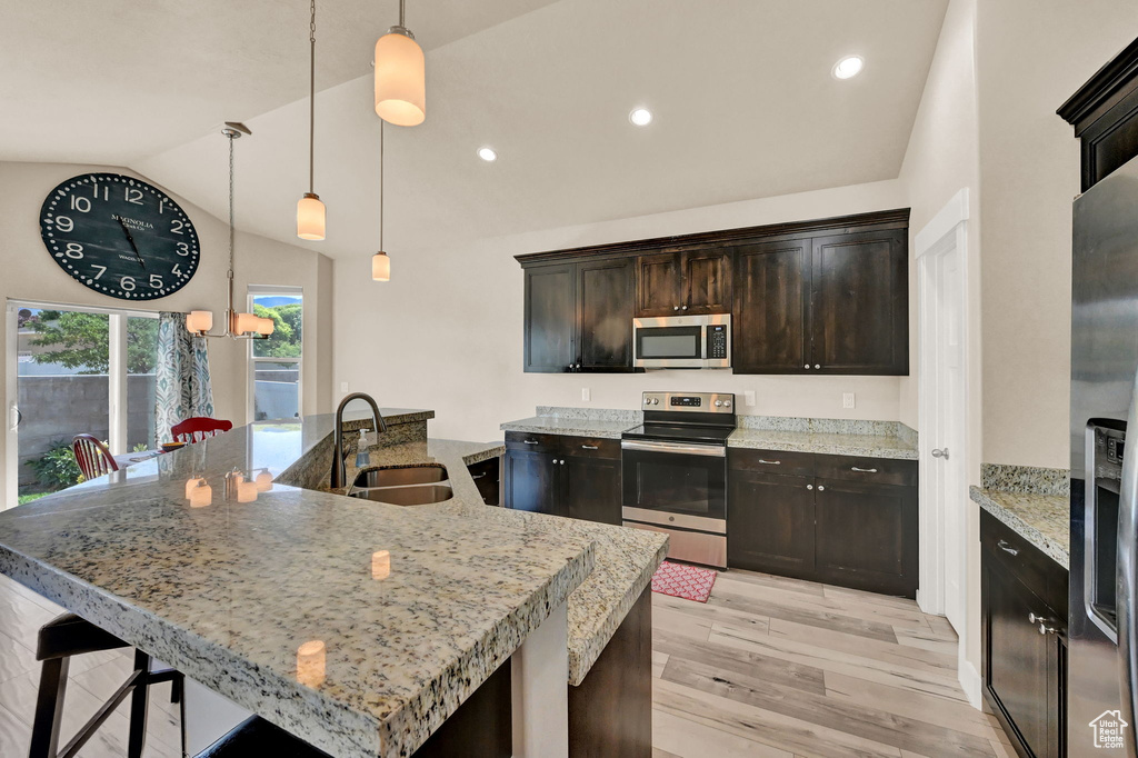 Kitchen featuring light hardwood / wood-style floors, appliances with stainless steel finishes, decorative light fixtures, dark brown cabinetry, and sink