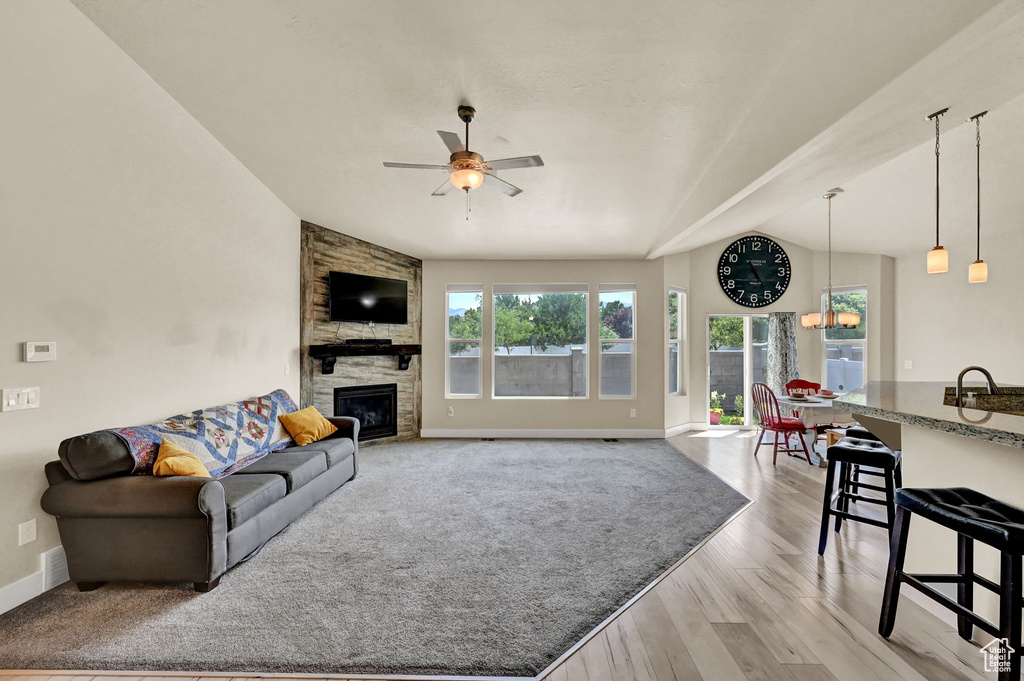 Living room featuring lofted ceiling, light wood-type flooring, ceiling fan, a stone fireplace, and sink