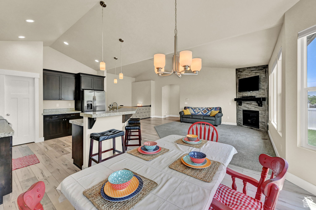 Dining area with a chandelier, light wood-type flooring, a stone fireplace, sink, and high vaulted ceiling