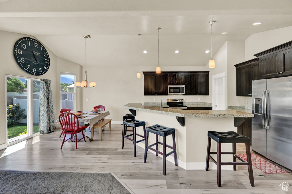 Kitchen featuring a breakfast bar area, light wood-type flooring, stainless steel appliances, hanging light fixtures, and dark brown cabinetry