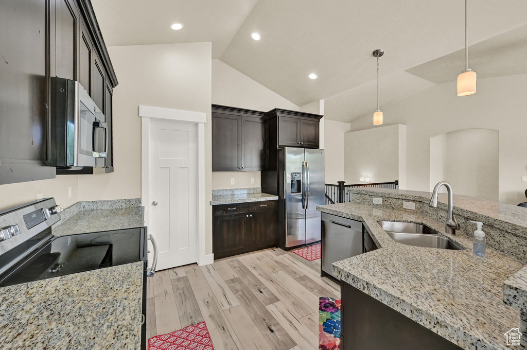 Kitchen with light hardwood / wood-style flooring, stainless steel appliances, sink, pendant lighting, and light stone counters