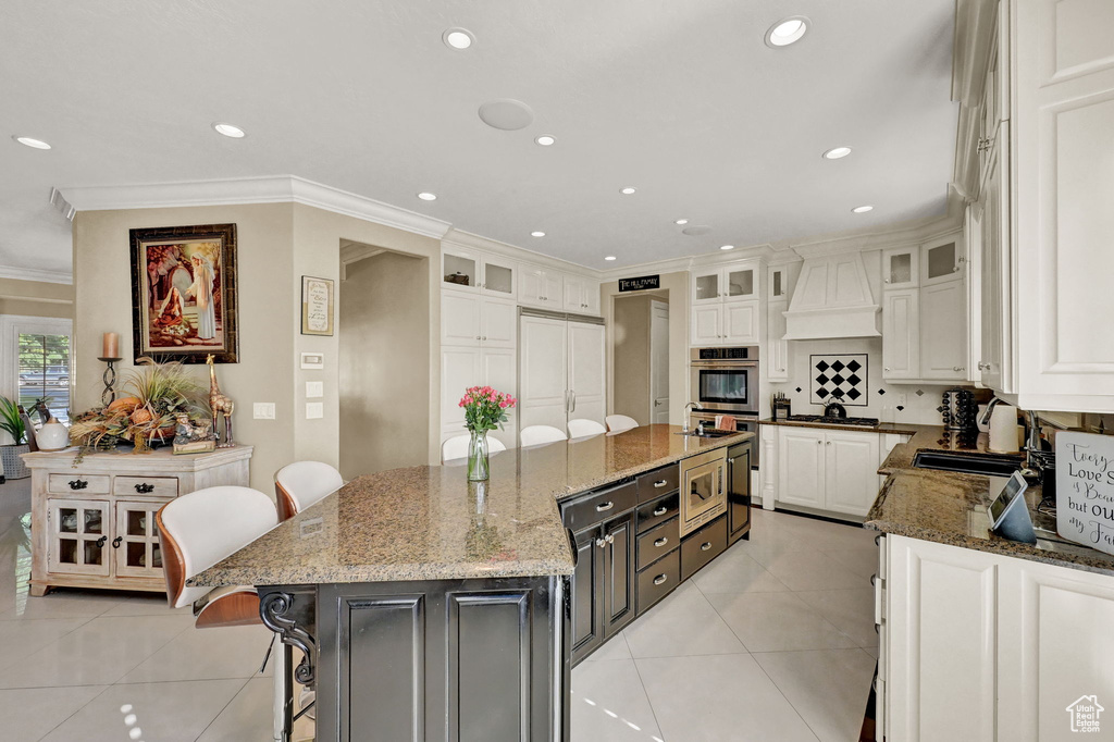 Kitchen with light tile patterned flooring, white cabinetry, a center island, premium range hood, and built in appliances