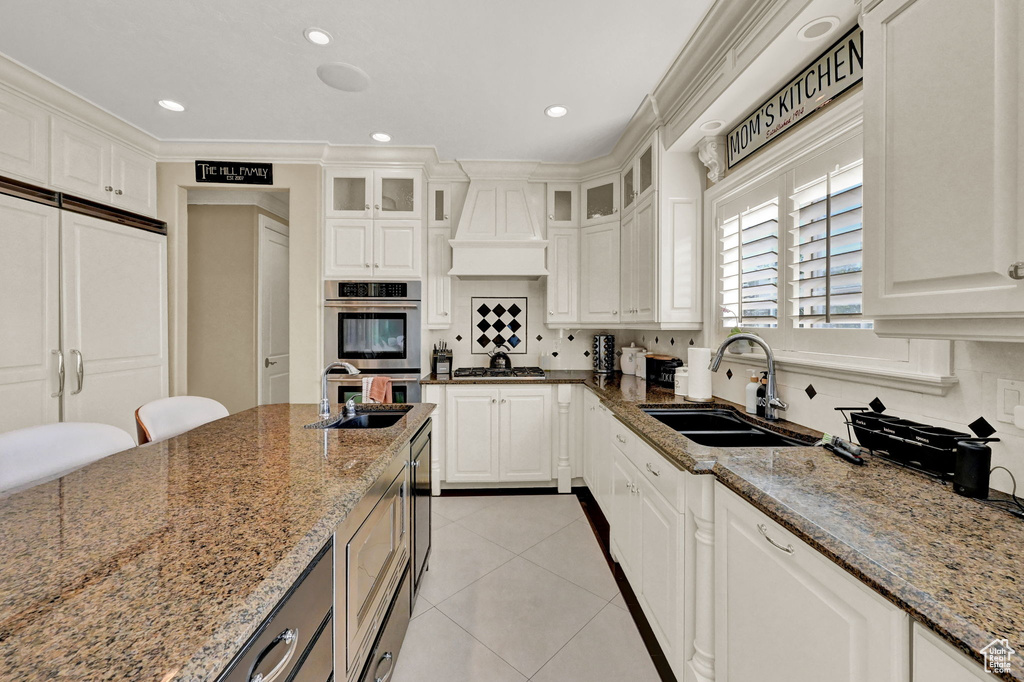 Kitchen featuring sink, custom exhaust hood, tasteful backsplash, and light stone countertops