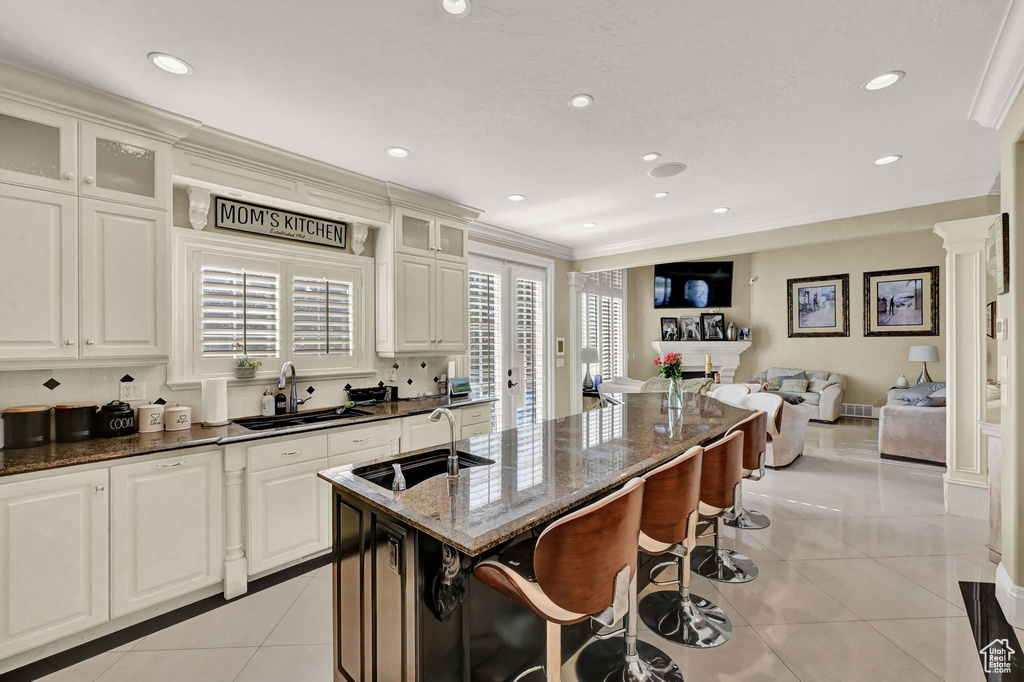 Kitchen with ornamental molding, sink, a breakfast bar, light tile patterned floors, and a kitchen island with sink