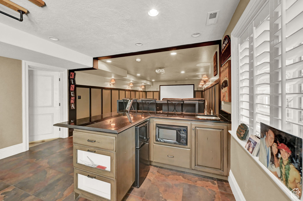 Kitchen featuring black microwave, dark tile patterned floors, a textured ceiling, and kitchen peninsula