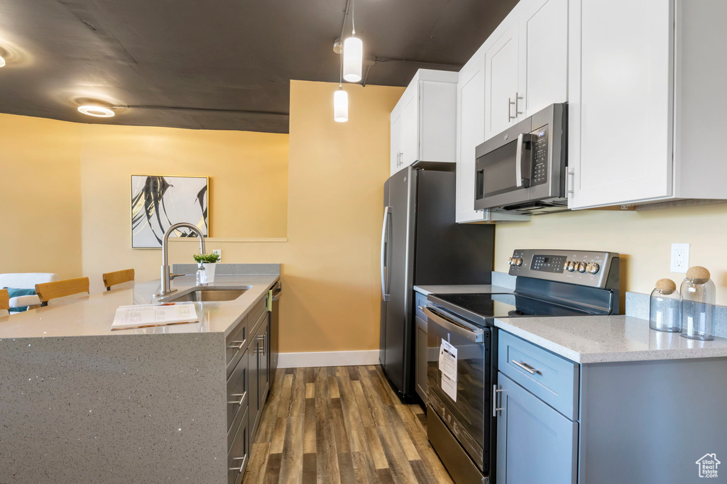 Kitchen featuring stainless steel appliances, sink, light stone counters, pendant lighting, and dark hardwood / wood-style floors