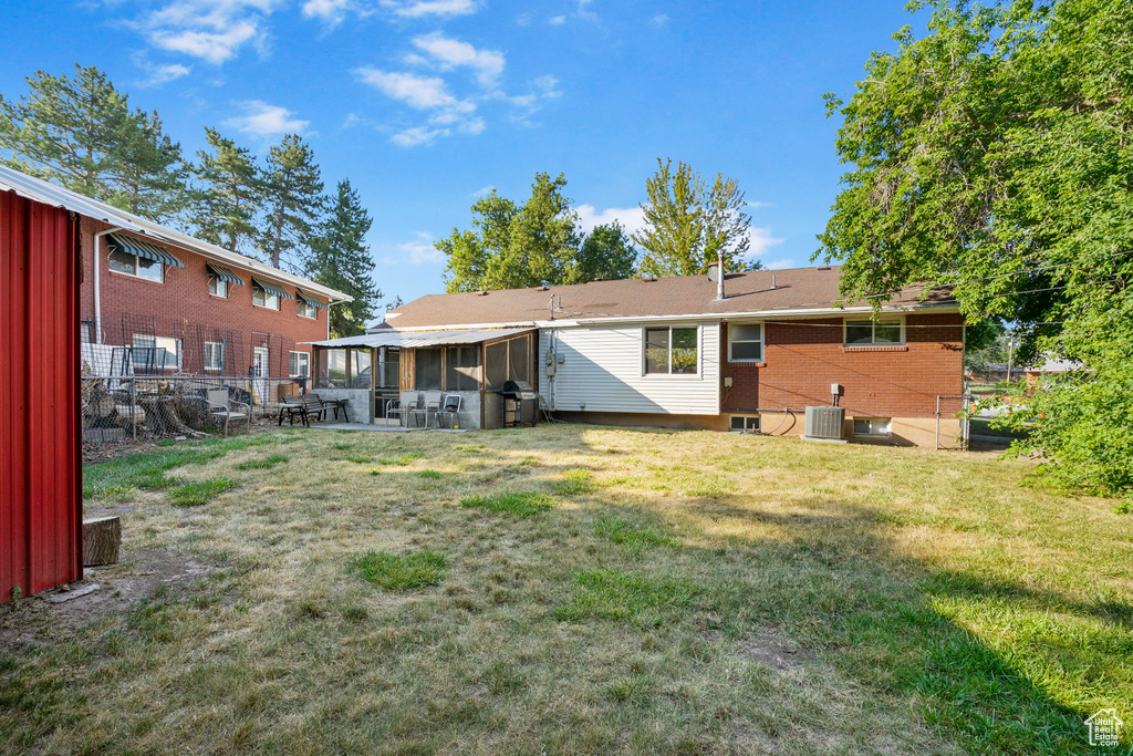 Rear view of house with central AC unit, a sunroom, and a lawn