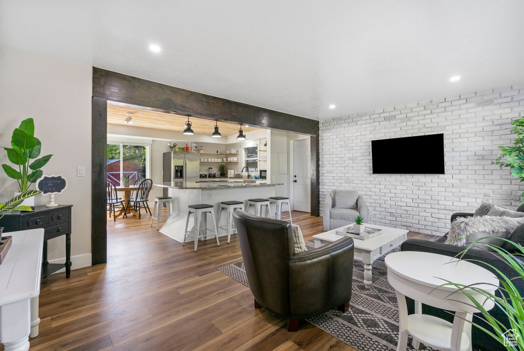 Living room featuring sink, brick wall, beamed ceiling, and dark wood-type flooring