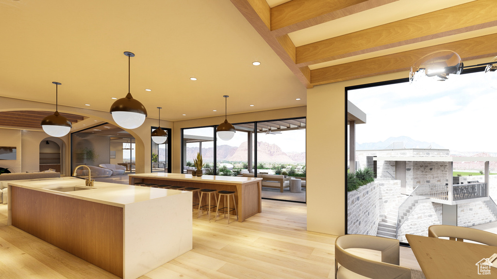 Kitchen with light hardwood / wood-style flooring, a mountain view, a kitchen island with sink, hanging light fixtures, and sink