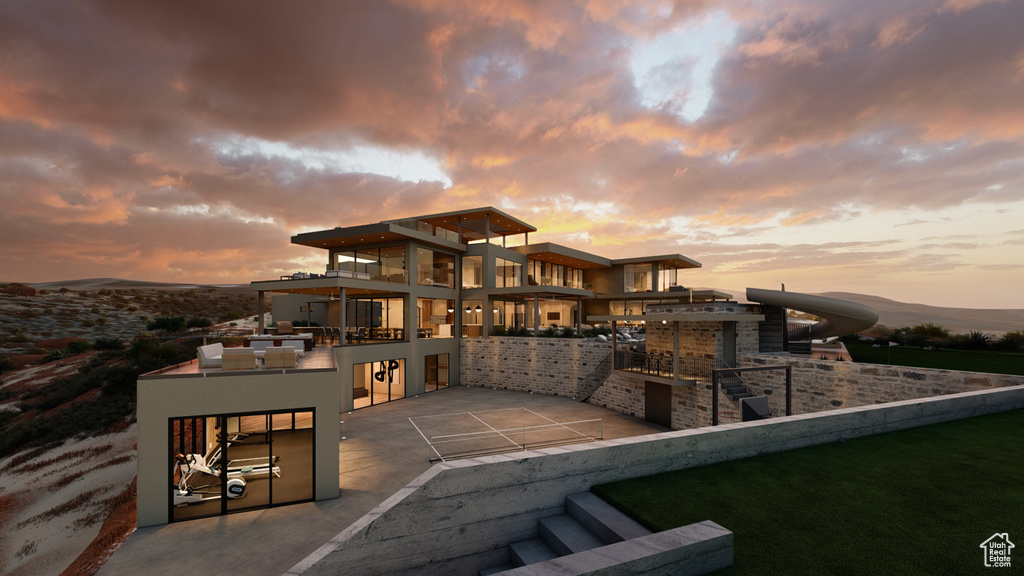 Back house at dusk featuring a balcony, a bar, a patio area, and exterior kitchen