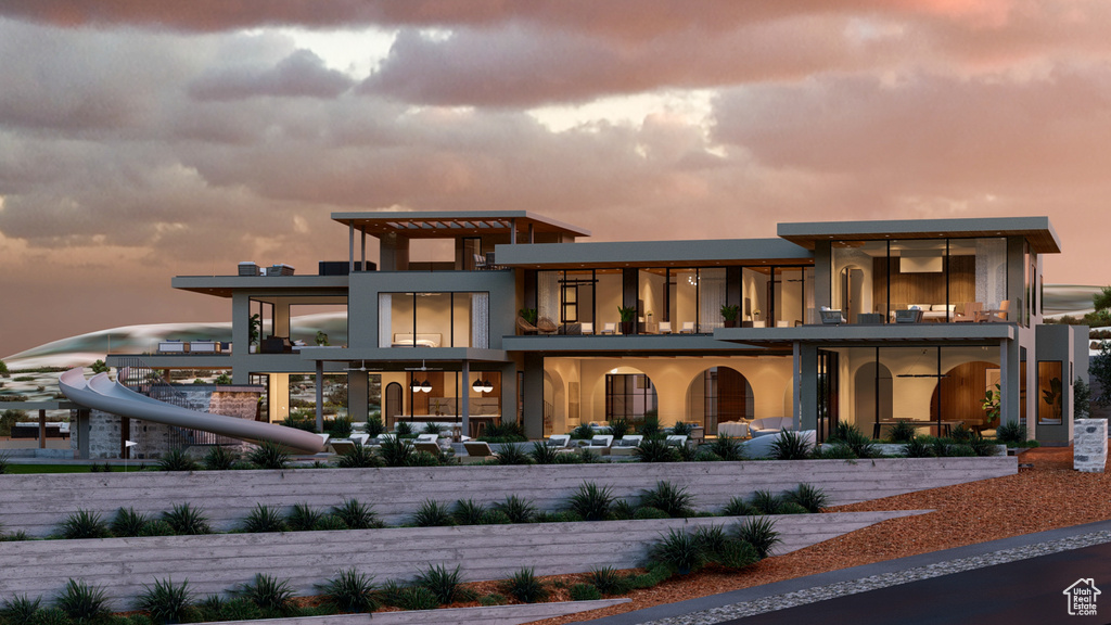 Back house at dusk with a pergola and a balcony