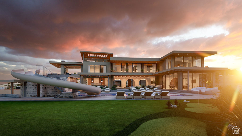 Back house at dusk featuring a balcony and a lawn