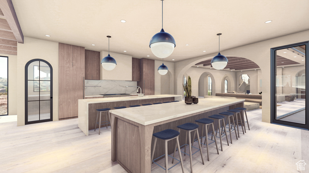 Kitchen featuring decorative light fixtures, light wood-type flooring, a kitchen bar, a kitchen island, and backsplash