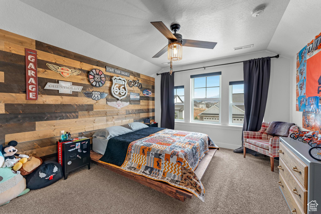 Carpeted bedroom with wood walls, lofted ceiling, ceiling fan, and a textured ceiling