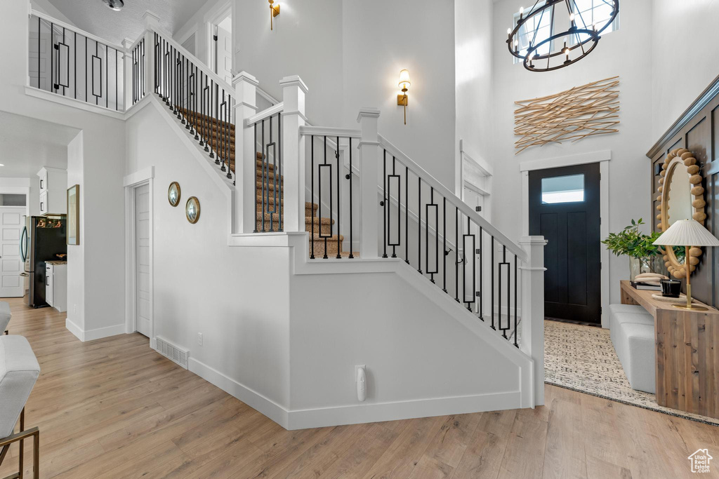 Entrance foyer with an inviting chandelier, light hardwood / wood-style flooring, and a towering ceiling