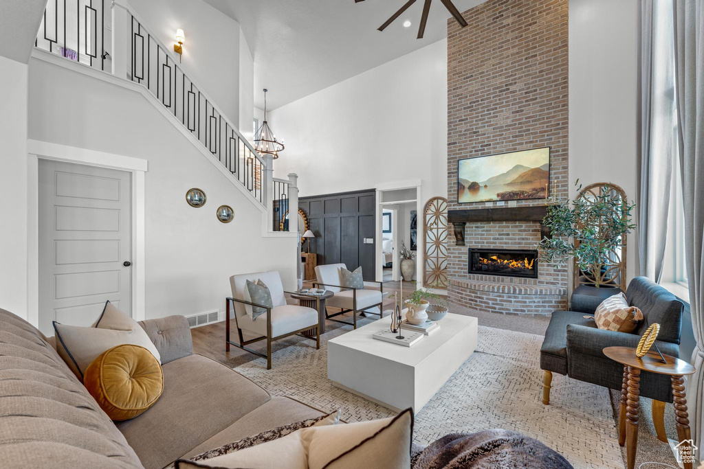 Living room featuring ceiling fan with notable chandelier, light wood-type flooring, a brick fireplace, and a towering ceiling