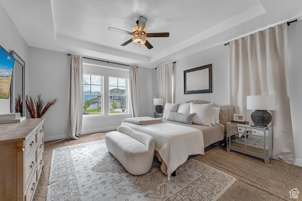 Carpeted bedroom featuring ceiling fan and a tray ceiling