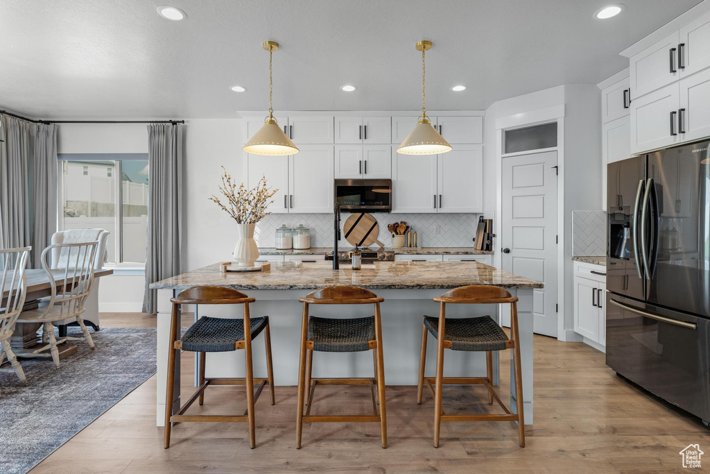 Kitchen featuring tasteful backsplash, stainless steel appliances, light stone countertops, a center island with sink, and light hardwood / wood-style flooring