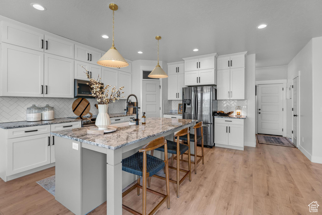 Kitchen featuring stainless steel appliances, white cabinets, decorative backsplash, an island with sink, and light hardwood / wood-style flooring