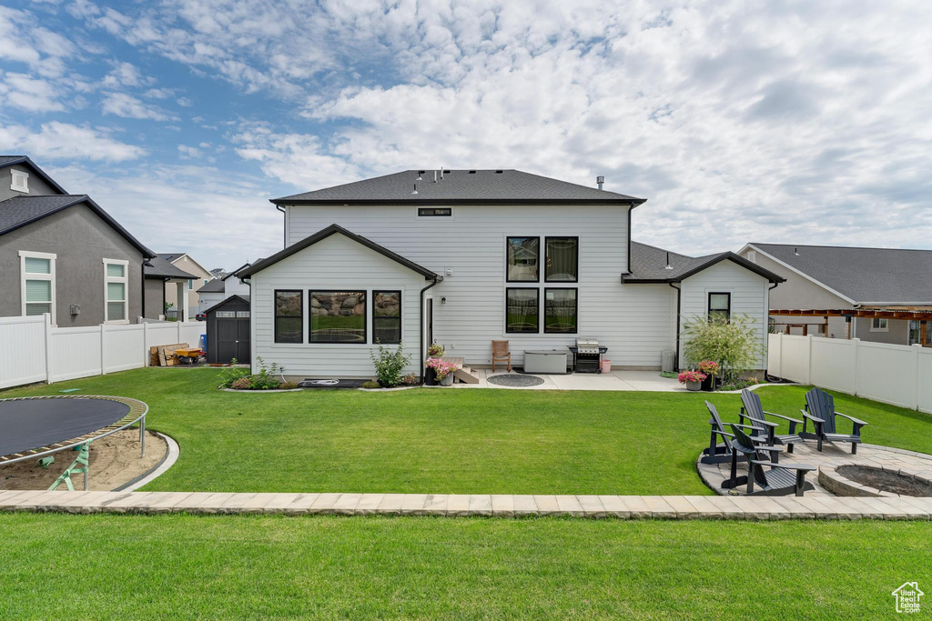 Rear view of house featuring a patio area, a yard, a trampoline, and a fire pit