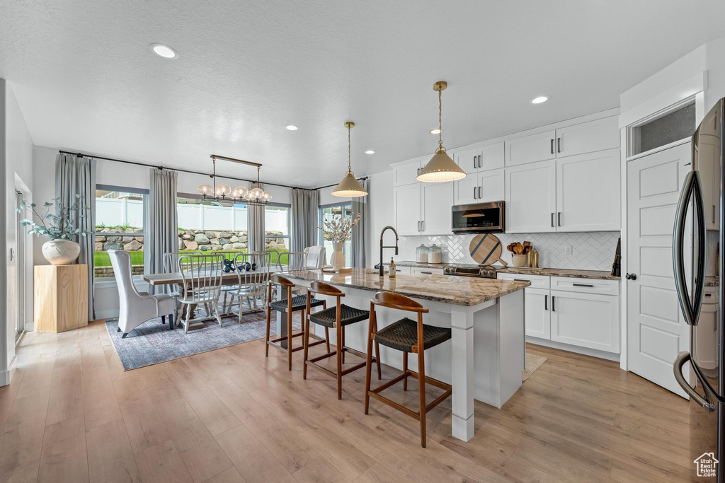 Kitchen with white cabinets, backsplash, light stone counters, an island with sink, and light hardwood / wood-style floors