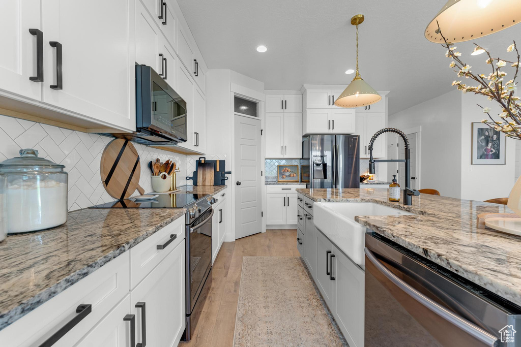 Kitchen with decorative light fixtures, white cabinetry, stainless steel appliances, decorative backsplash, and light wood-type flooring