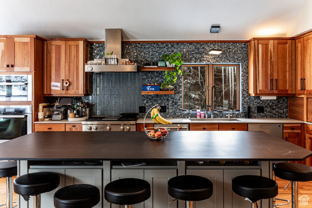 Kitchen with wall chimney range hood, stainless steel appliances, sink, a kitchen island, and backsplash