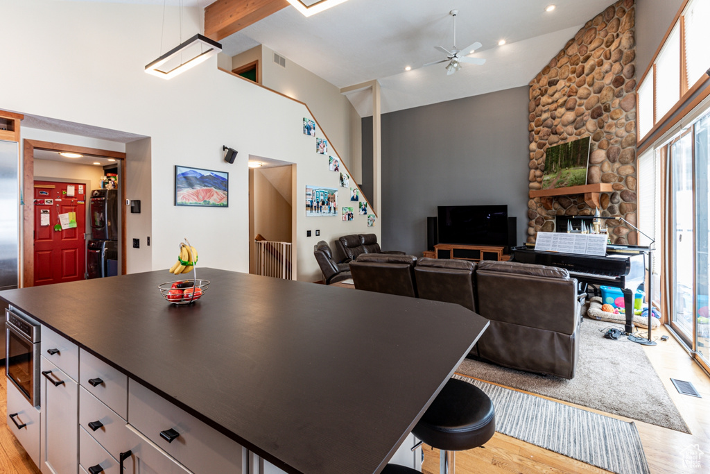 Kitchen with stainless steel oven, ceiling fan, light wood-type flooring, beam ceiling, and a stone fireplace