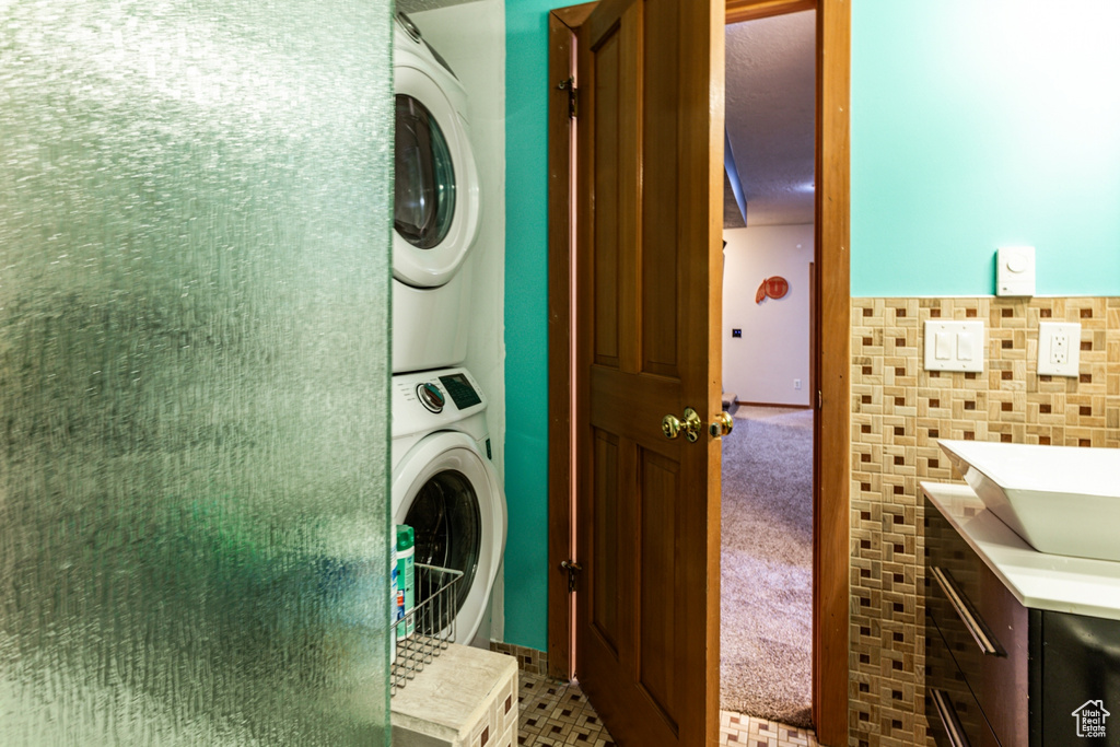 Laundry area featuring sink, tile patterned flooring, stacked washer and dryer, and tile walls