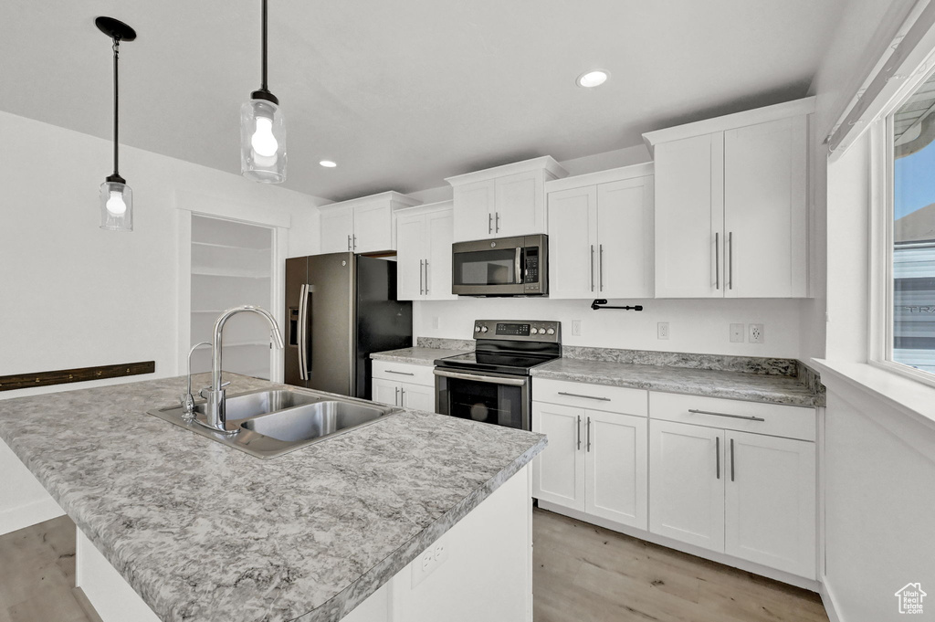 Kitchen featuring light hardwood / wood-style flooring, an island with sink, stainless steel appliances, decorative light fixtures, and sink