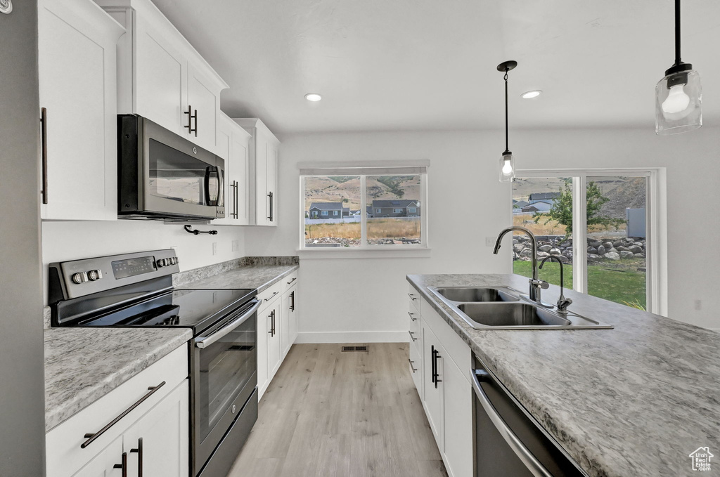 Kitchen featuring light hardwood / wood-style flooring, stainless steel appliances, white cabinets, sink, and decorative light fixtures