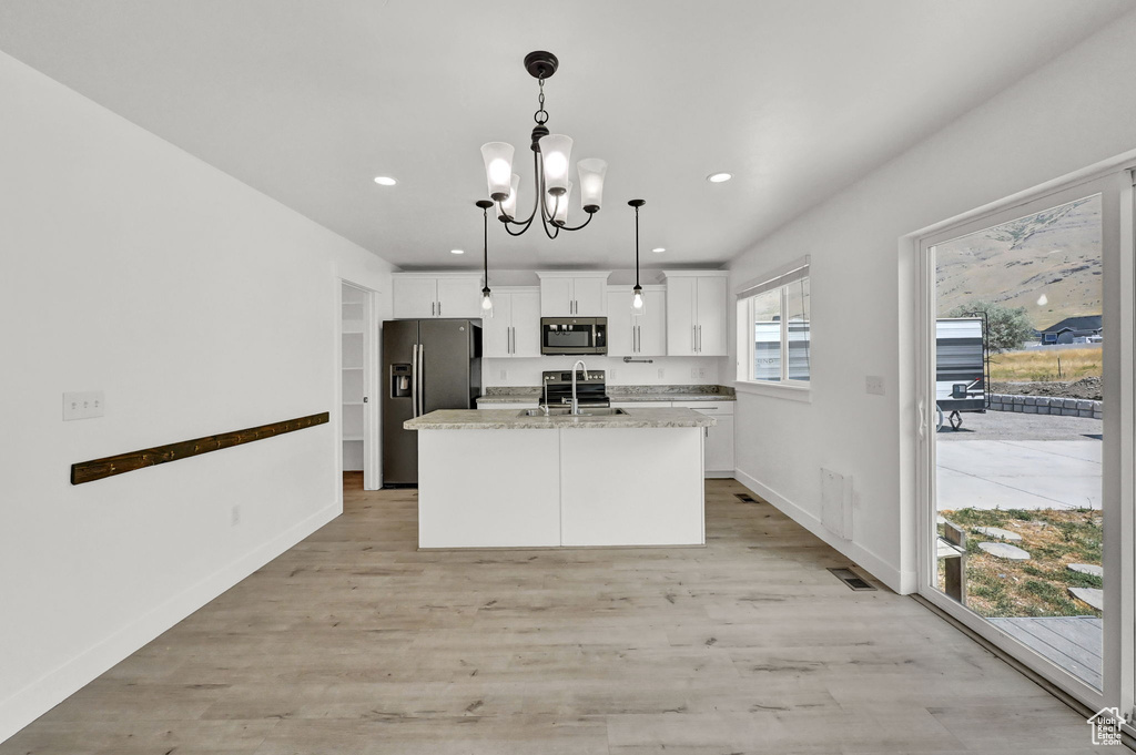 Kitchen with light hardwood / wood-style floors, appliances with stainless steel finishes, white cabinetry, and a kitchen island with sink