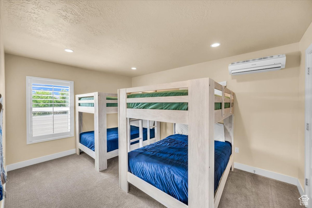 Carpeted bedroom with a wall mounted air conditioner and a textured ceiling