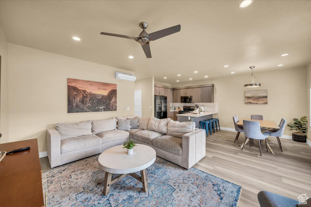 Living room with light hardwood / wood-style floors, a wall unit AC, and ceiling fan