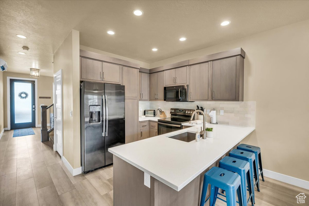 Kitchen with sink, light hardwood / wood-style floors, appliances with stainless steel finishes, kitchen peninsula, and backsplash