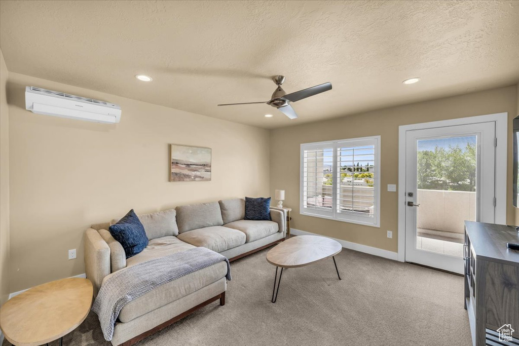 Living room featuring a wall mounted air conditioner, a textured ceiling, ceiling fan, and light colored carpet