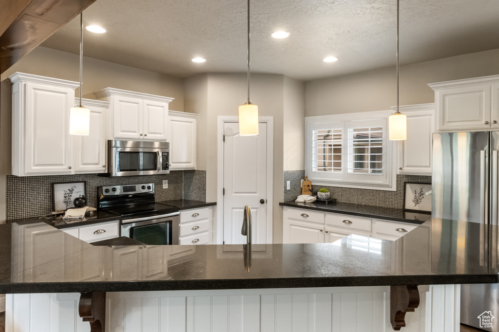 Kitchen with white cabinets, backsplash, a breakfast bar, and appliances with stainless steel finishes