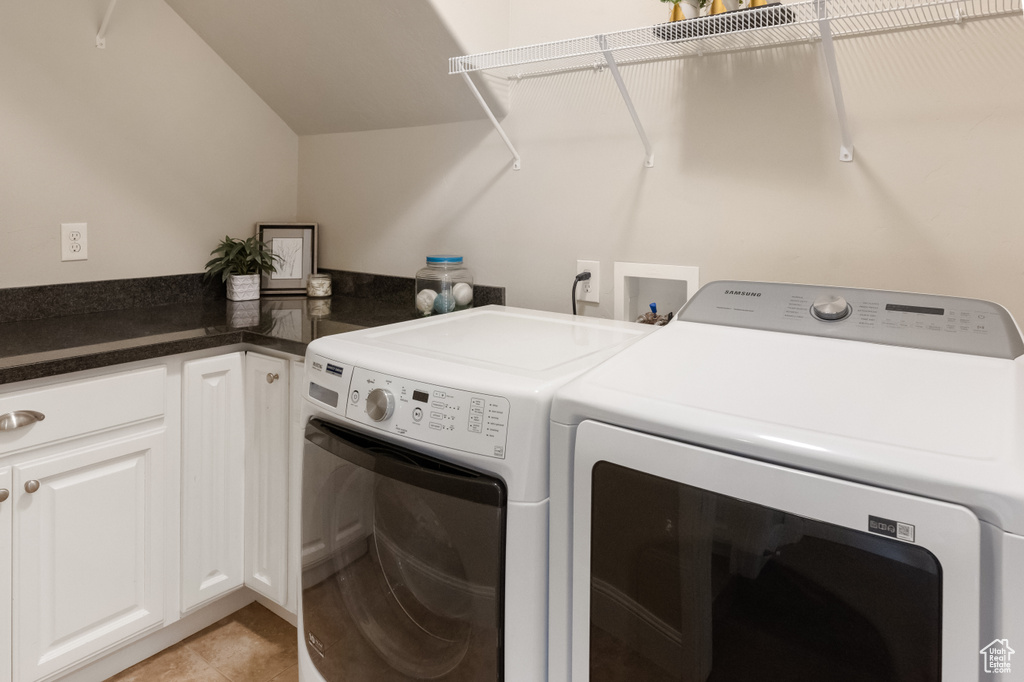 Laundry room featuring light tile patterned flooring, washing machine and dryer, and cabinets