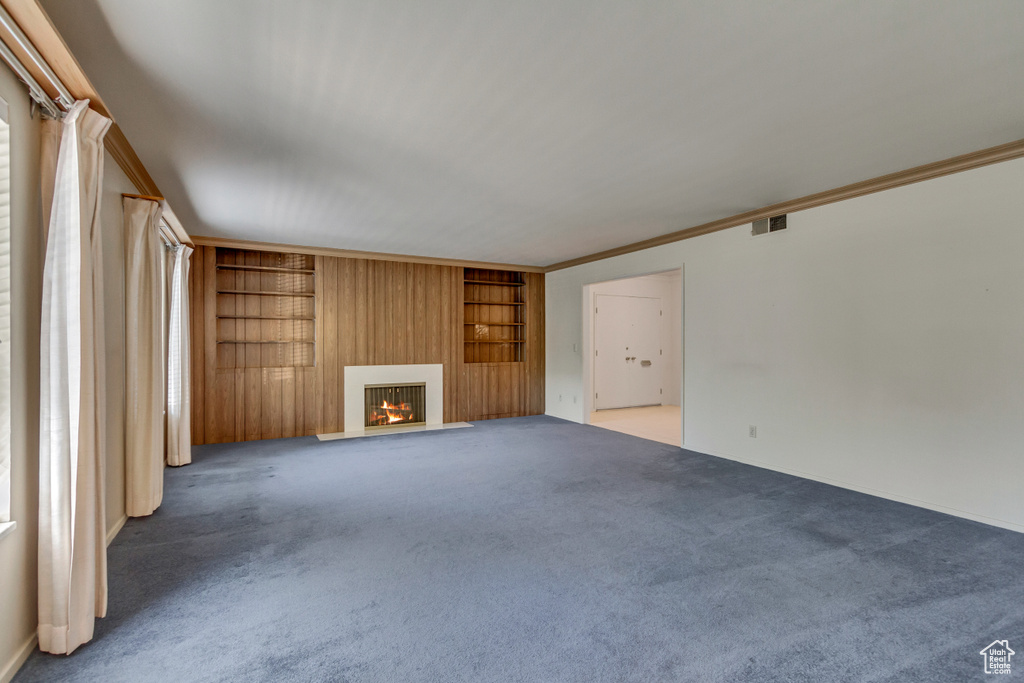 Unfurnished living room with built in shelves, carpet, and crown molding