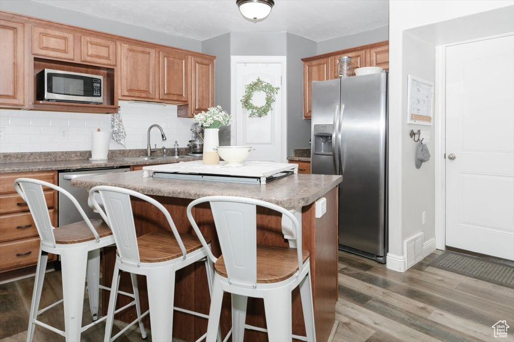 Kitchen with a center island, dark hardwood / wood-style floors, stainless steel appliances, decorative backsplash, and sink