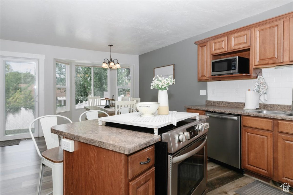 Kitchen with a chandelier, backsplash, dark wood-type flooring, a kitchen island, and appliances with stainless steel finishes