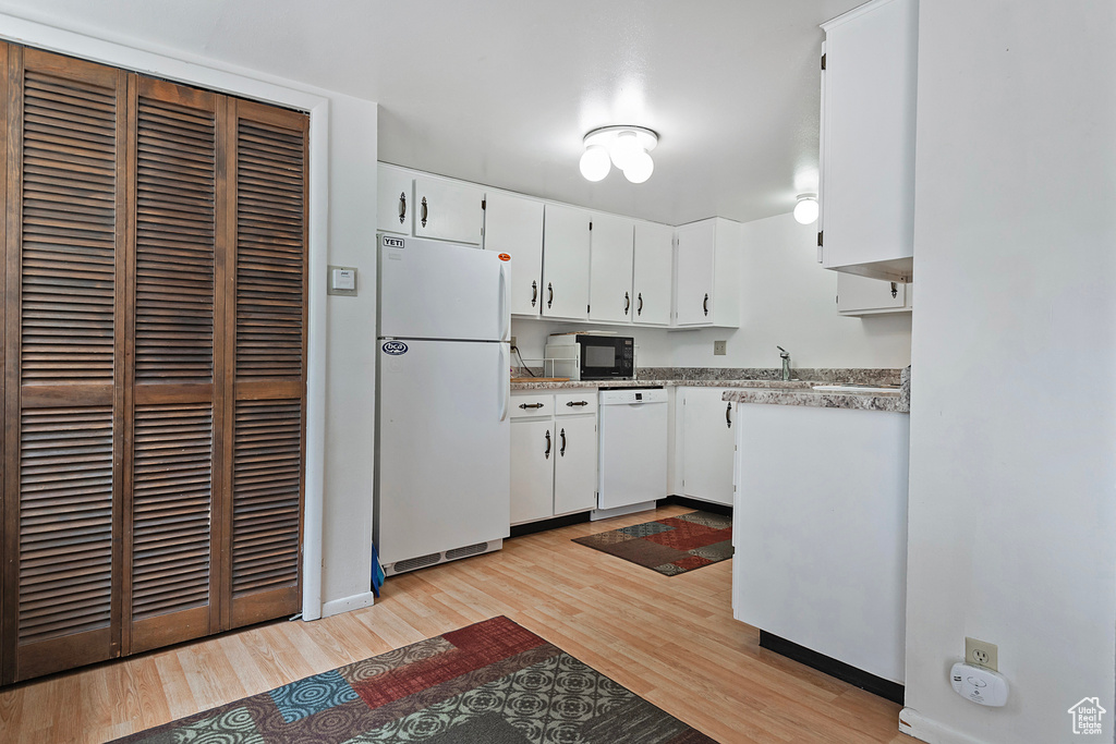 Kitchen with sink, light wood-type flooring, white appliances, and white cabinets