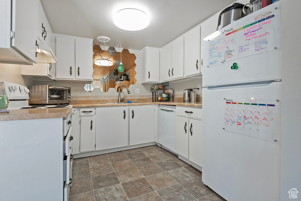 Kitchen featuring sink, white cabinetry, dark tile patterned floors, and white appliances