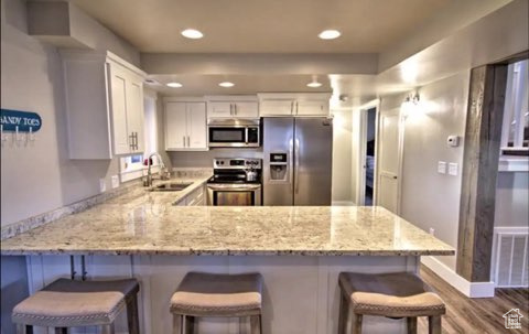 Kitchen featuring white cabinetry, hardwood / wood-style flooring, sink, appliances with stainless steel finishes, and kitchen peninsula