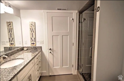 Bathroom with tile patterned flooring, a shower with door, and vanity