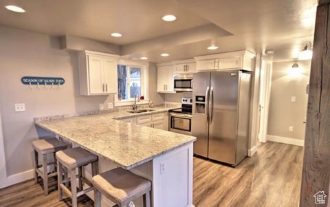 Kitchen featuring kitchen peninsula, appliances with stainless steel finishes, white cabinets, and light wood-type flooring