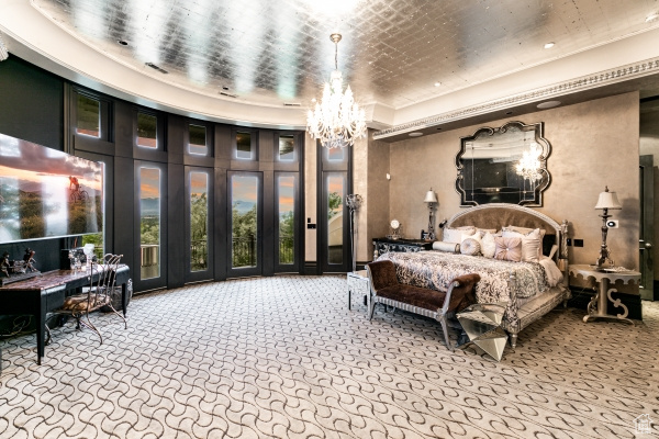 Carpeted bedroom featuring an inviting chandelier, french doors, and a tray ceiling