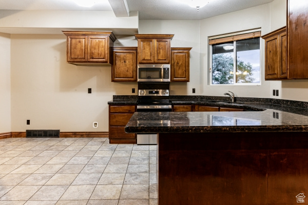 Kitchen featuring dark stone countertops, appliances with stainless steel finishes, kitchen peninsula, and light tile patterned flooring